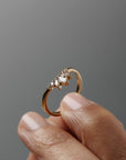 Close-up of a women's finger holding the Trillium curved gold wedding band, featuring marquise and round diamonds.
