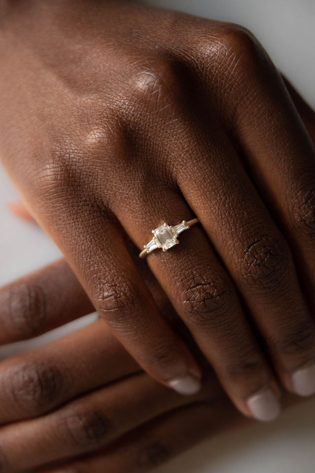 Model wearing the Three Stone Adele Solitaire Engagement Ring in yellow gold by Fluid Jewellery