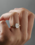 Close-up of the Cora split shank milgrain engagement solitaire worn on a woman's finger, featuring an emerald cit diamond and round diamond accents.