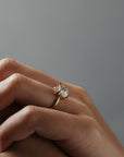 Stylized close-up of Asscher cut diamond claw solitaire worn on a woman's finger, highlighting the delicate floral scroll detailing along the side of the low-profiled setting. 