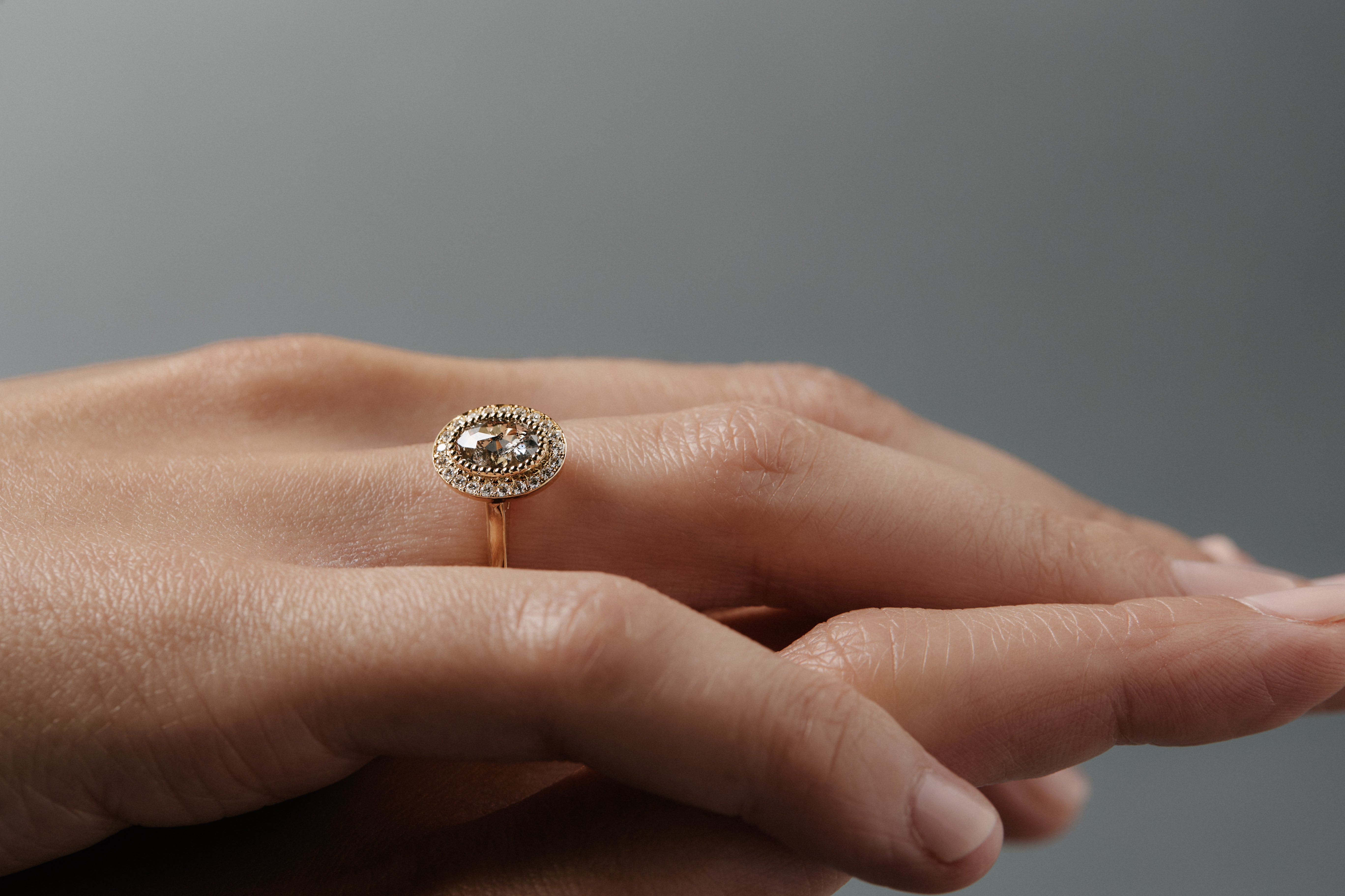 Stylized close-up pf crossed women's hands wearing the Aura halo solitaire with a change-toned Australian salt and pepper rose cut diamond and round Canadian diamonds.