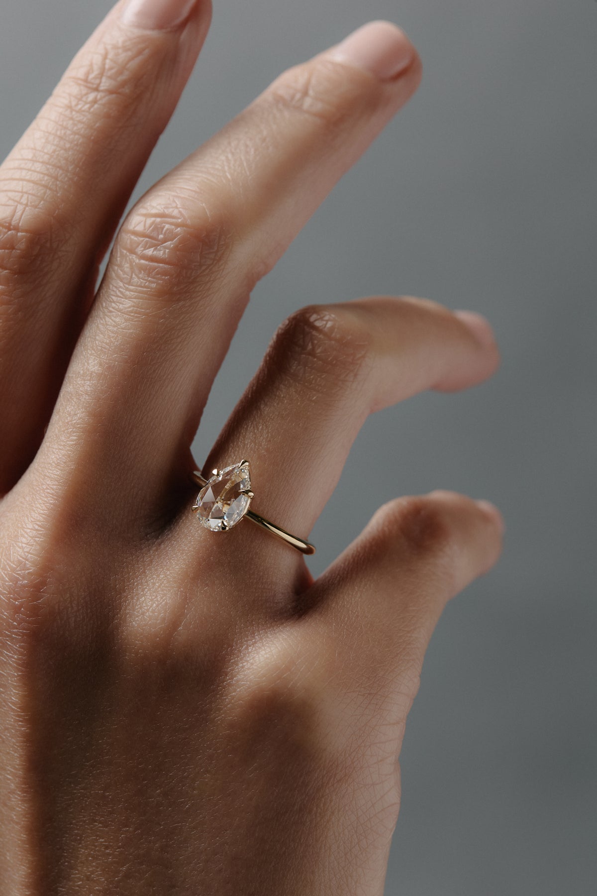 Close-up of a woman wearing the Avery pear shaped rose cut diamond solitaire  engagement ring on her hand.