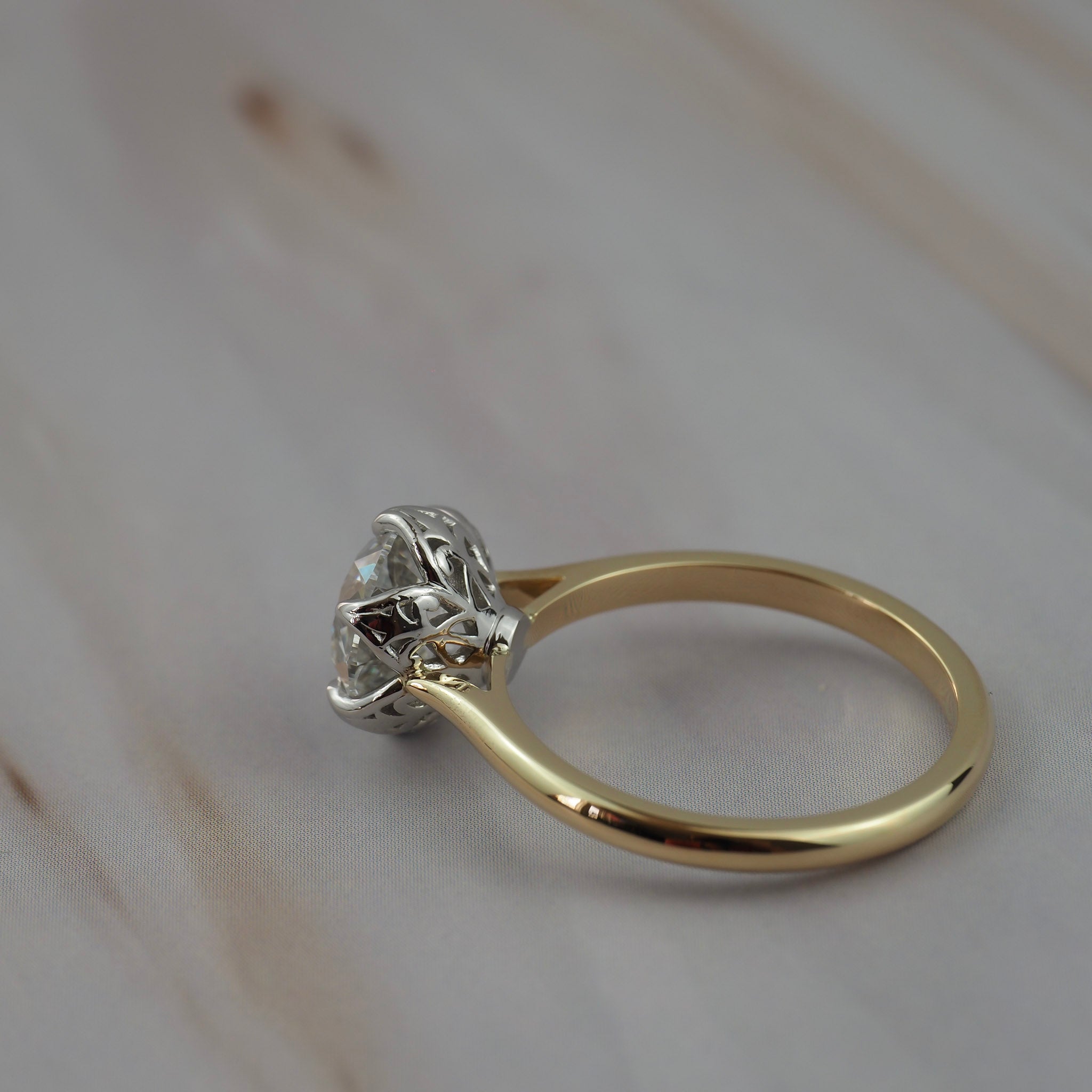 Close-up of the side profile of the Cala solitaire showing the two-tone platinum setting and gold band with antique filigree inspired details.