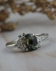 Celeste cluster engagement ring featuring a natural teal sapphire surrounded by diamonds crafted in a white gold setting.