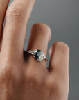Close-up of a woman wearing the Celeste teal sapphire and diamond cluster engagement ring on her finger. 