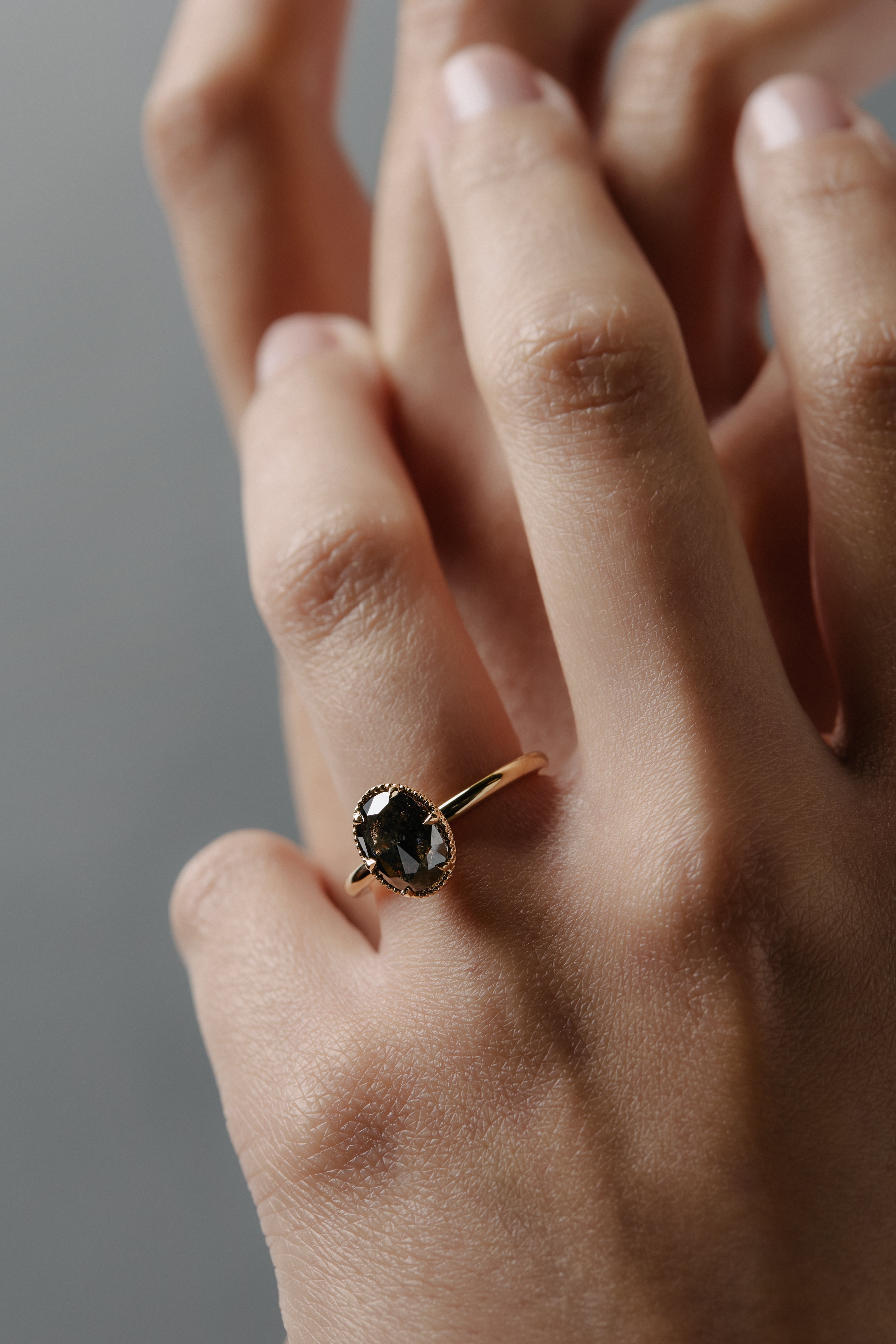 Close-up of the Elanor salt and pepper oval diamond six-claw solitaire worn on a woman's finger.