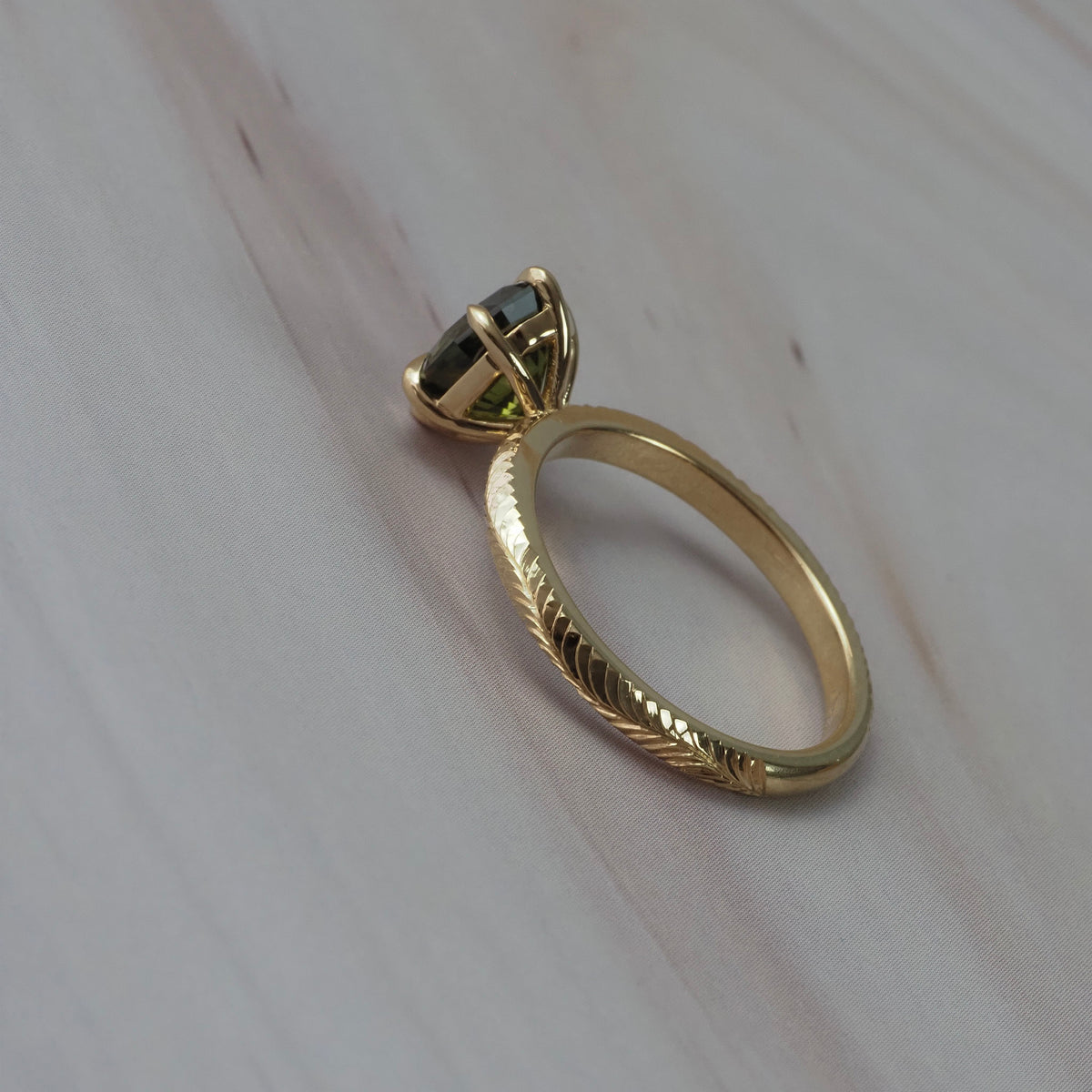 Back view of the Fern hand-engraved solitaire showing the detailed Fairmined gold band and setting around the step-cut oval green sapphire.