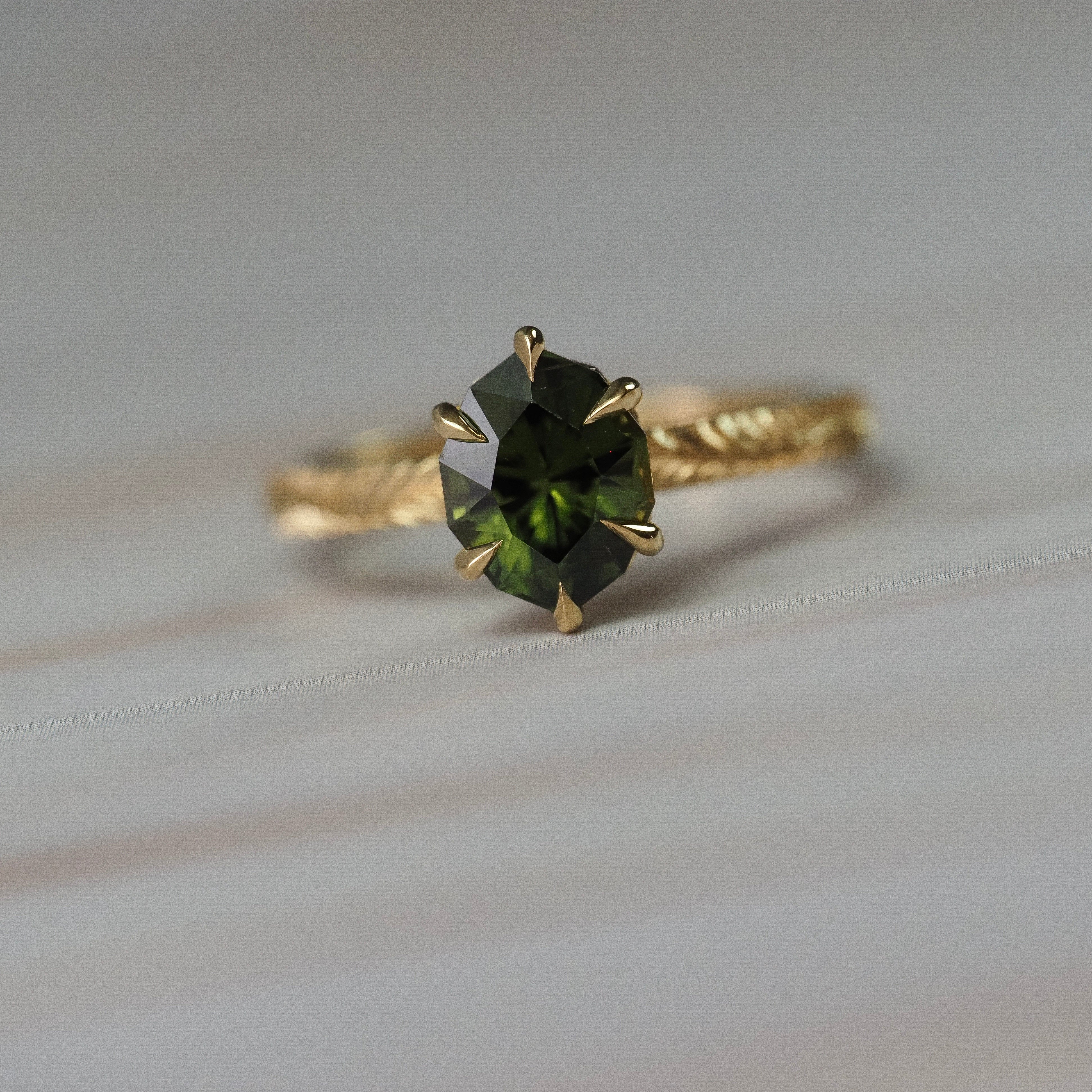 Fern hand engraved solitaire engagement ring featuring a step-cut oval green sapphire in Fairmined gold.