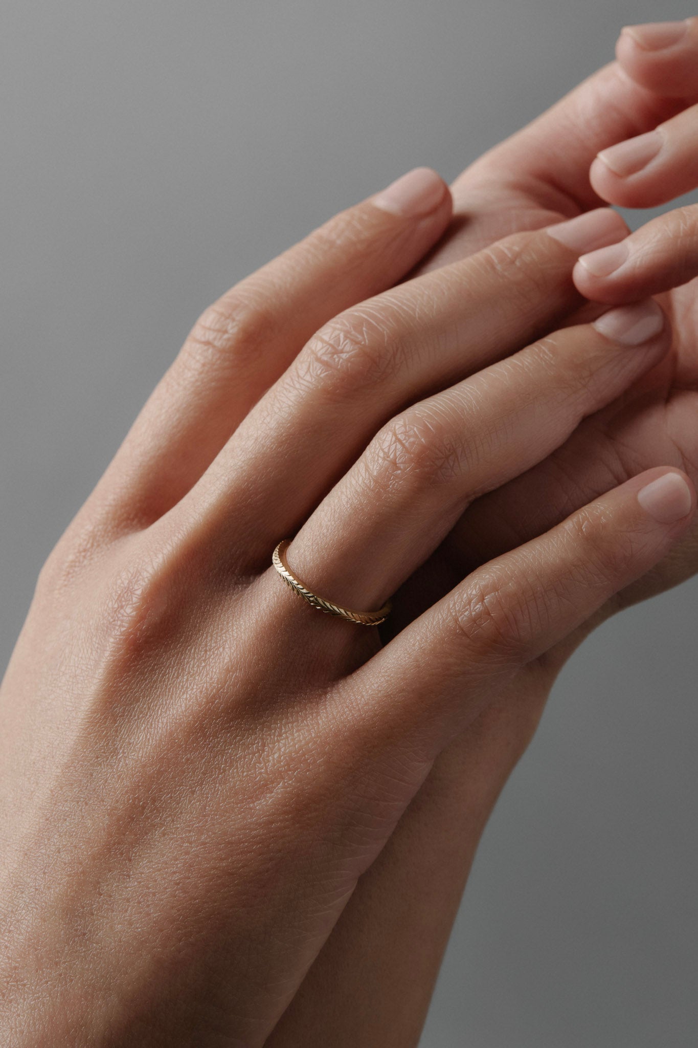 Hand-engraved fern pattern on a thin Fairmined yellow gold wedding band worn on a women's finger.