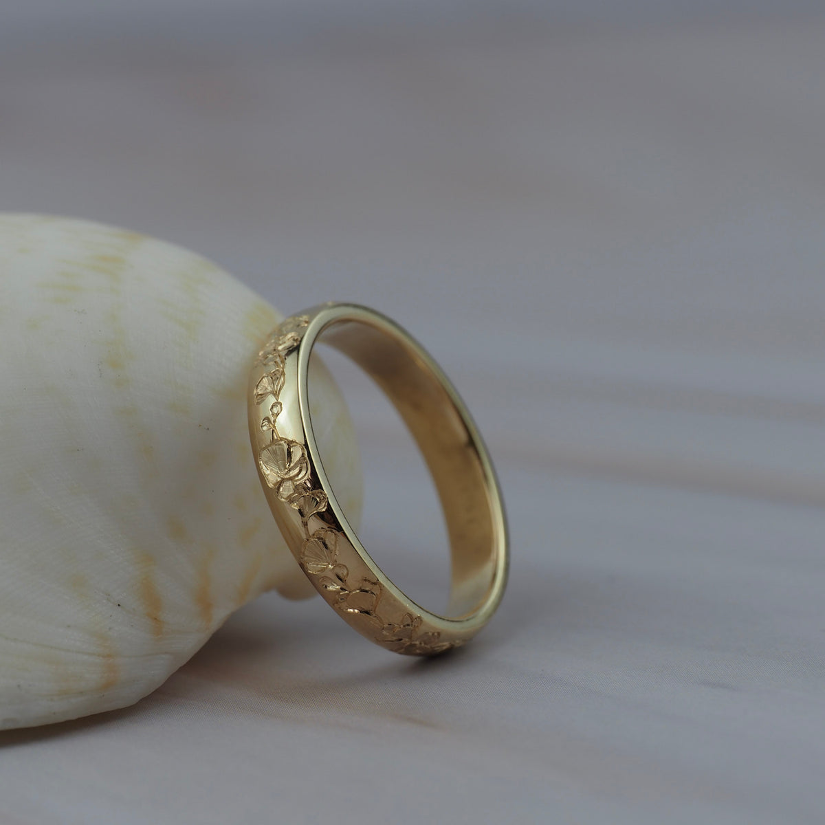 Close-up detail of hand engraved poppy flowers on a Fairmined yellow gold band.