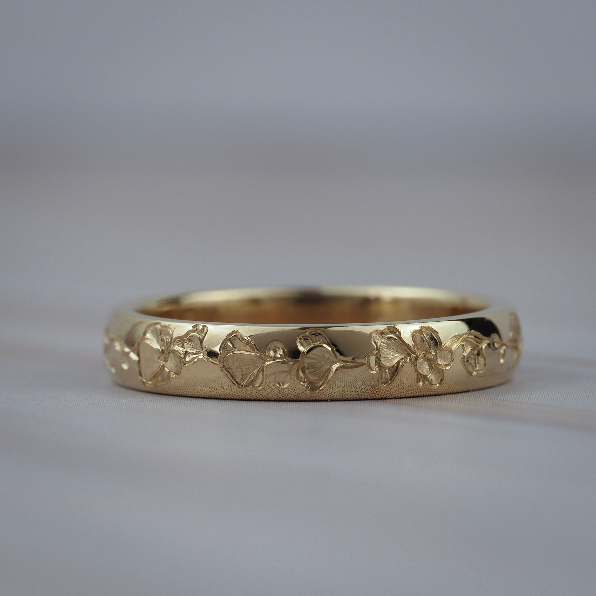 Close-up of hand engraved poppy flowers on a Fairmined yellow gold wedding band.