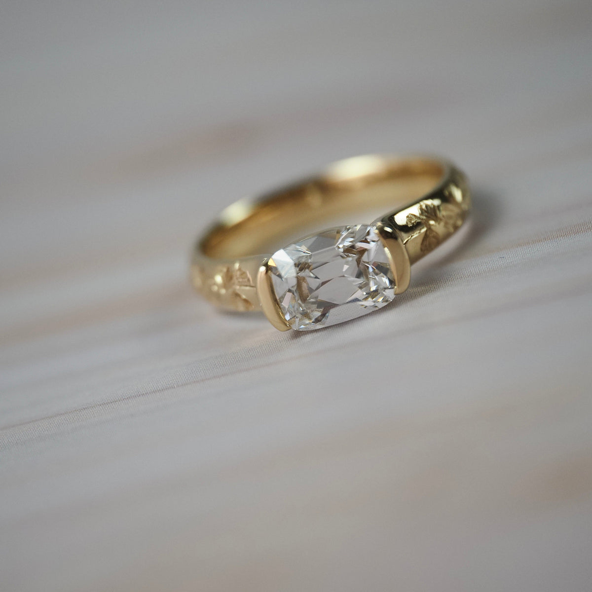Magnolia hall-bezel solitaire featuring an elongated Old European cushion cut diamond with hand engraved magnolia flowers along the band.