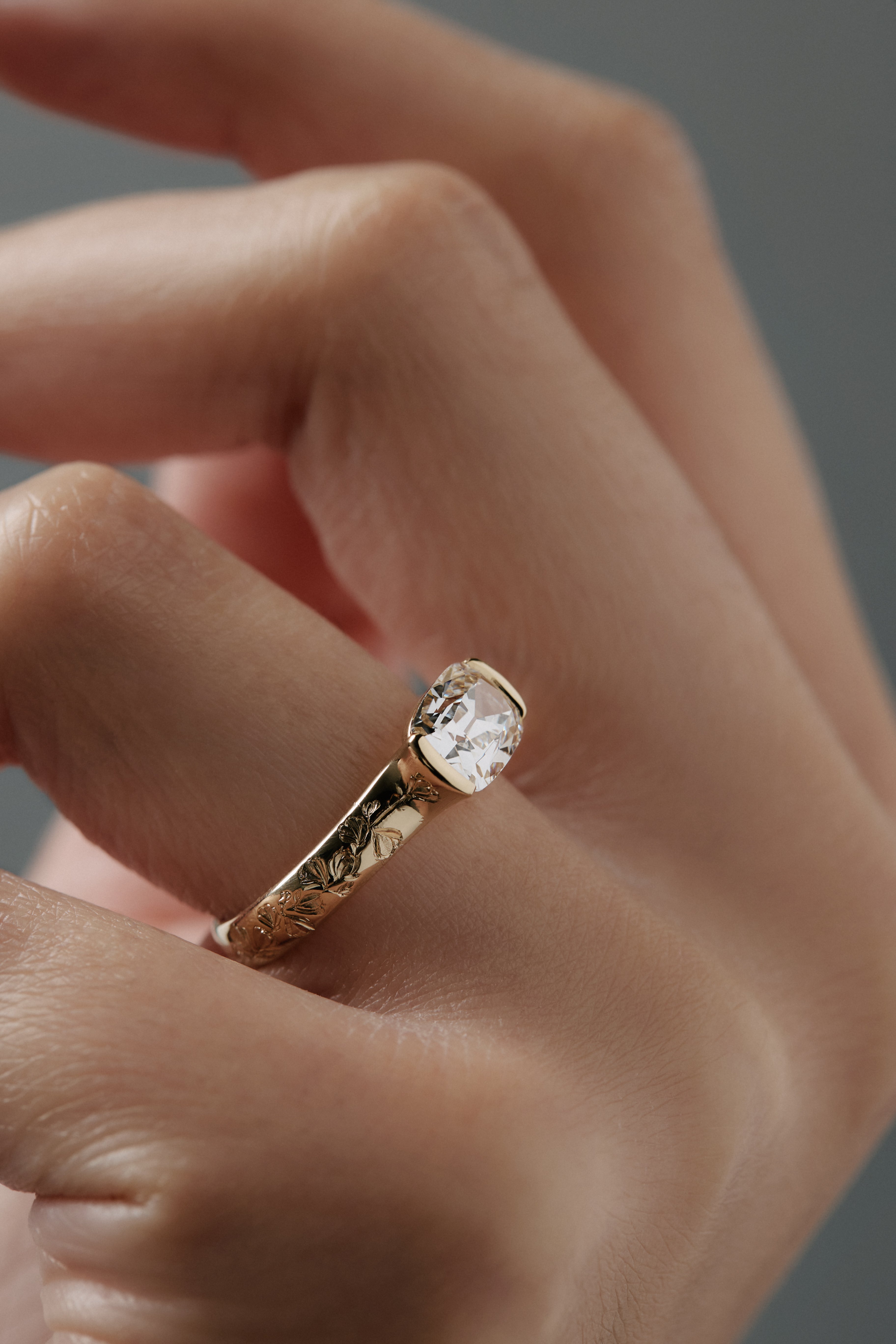 Close-up side view of the Magnolia half bezel solitaire on a woman's finger, highlighting  the hand engraved magnolia flowers and detailed diamond setting.
