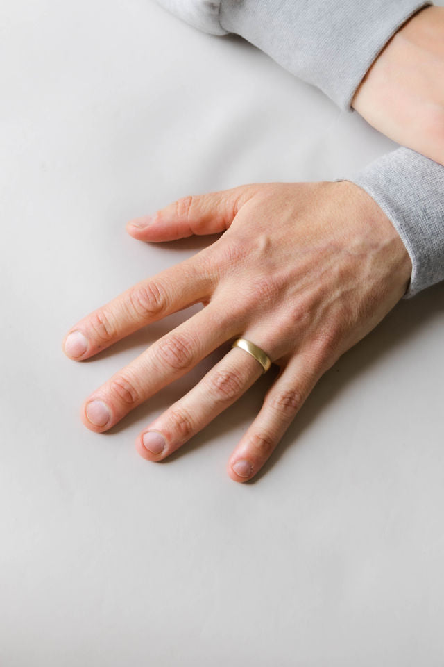 Close up of model hand wearing the mens Half Round wedding band in gold 2