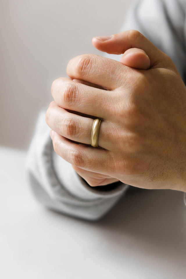 Close up of models hand wearing the mens Milgrain wedding band in gold