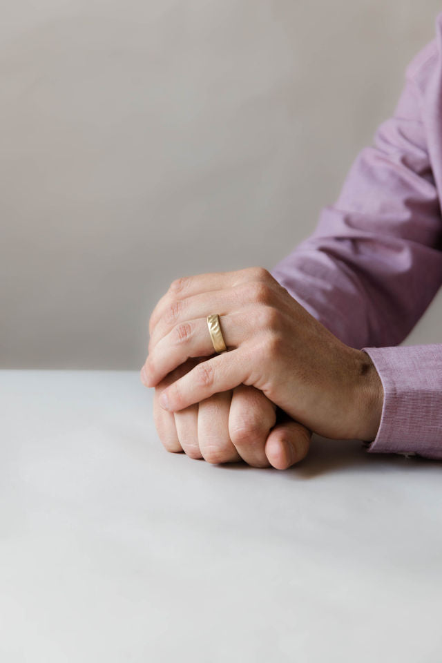 Close up of model hand wearing the mens Wave wedding band in yellow gold