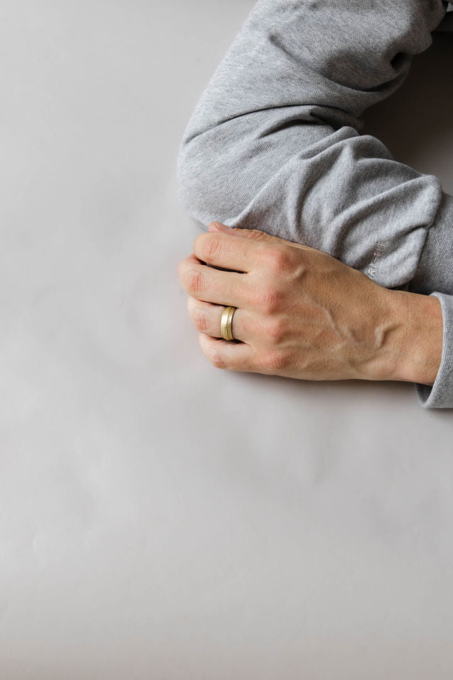 Close up of model hand wearing the mens Woodgrain wedding band in yellow gold