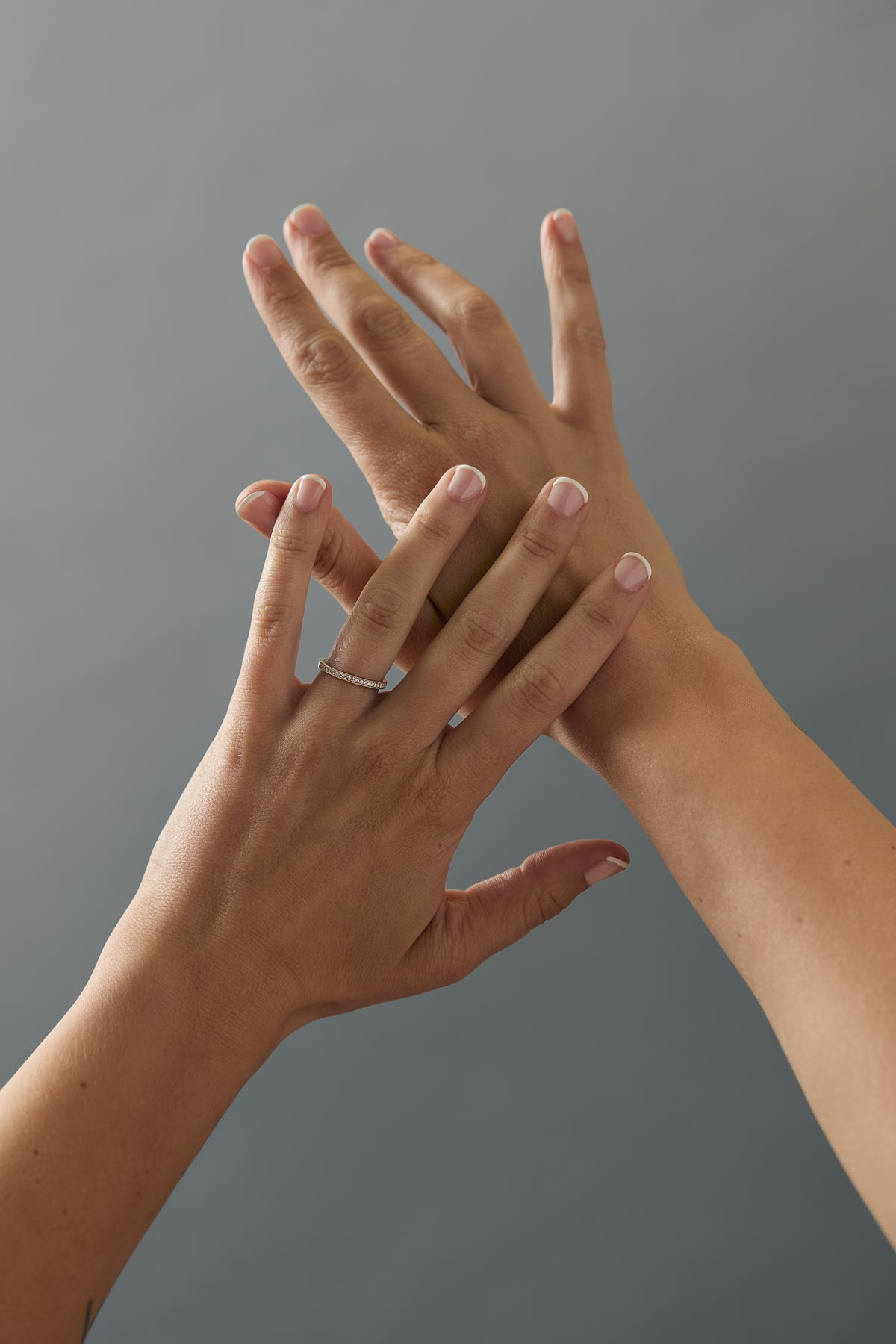 Milgrain Fairmined gold wedding band with Canadian diamonds shown on crossed women's hands.