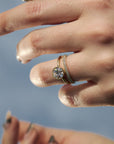 Close-up of a handcrafted milgrain Fairmined gold wedding band paired with the Flora solitaire engagement ring on a woman's hand.