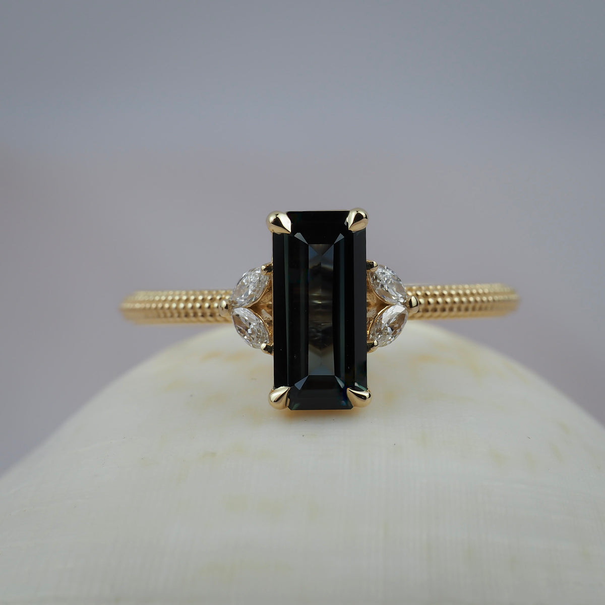 Millie cluster solitaire engagement featuring a rectangular lintel sapphire, marquise diamonds, and a migraines beaded gold band. 