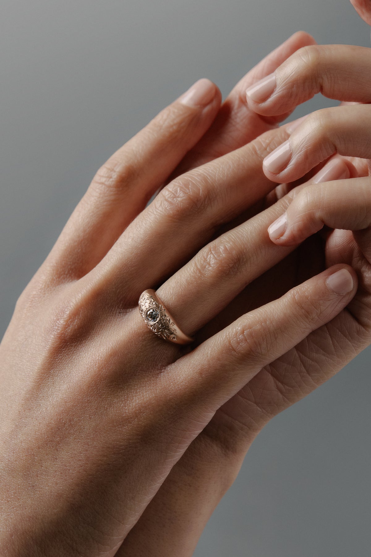 Close-up of the Mrs. Erykah hand engraved floral bombe engagement ring in Fairmined gold with a Canadian diamond, worn on a woman's finger.