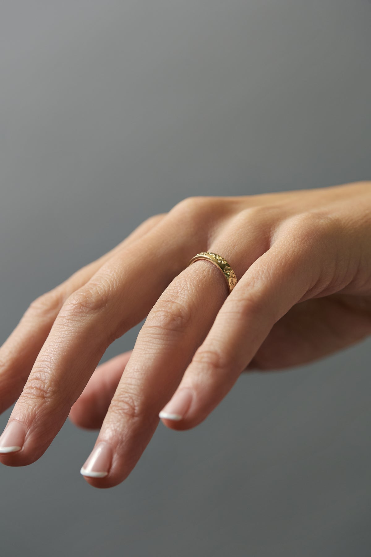 Close-up of hand engraved poppy  flowers on a Fairmined yellow gold band worn on women's hand.