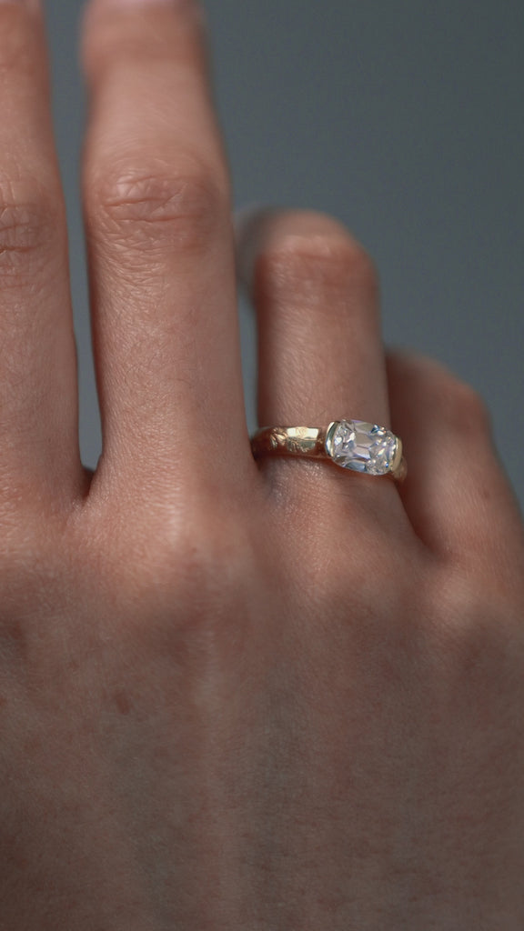Close-up video of a woman wearing the Magnolia half bezel solitaire, featuring an elongated Old European cushion cut diamond and hand engraved magnolia flowers. 