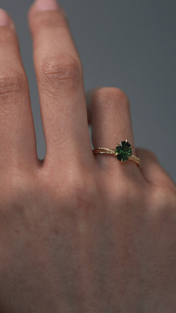 Close-up video of a woman wearing the Fern hand engraved solitaire in Fairmined gold, showcasing the step-cut oval green sapphire and detailed gold band.