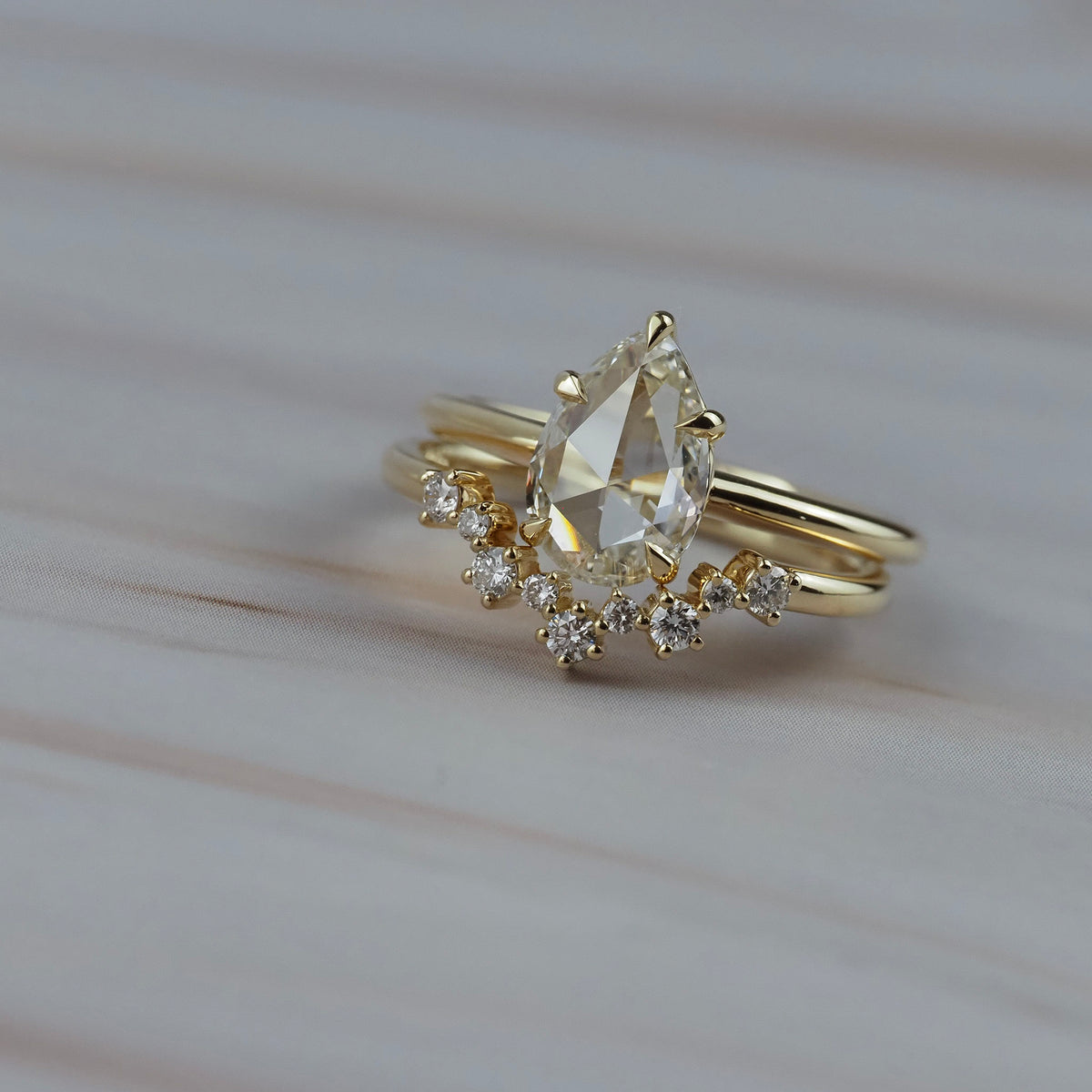 Close-up of the Snowflake curved diamond wedding band paired with a pear-shaped diamond engagement ring. 