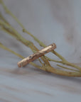 Starlight  hammered rose gold wedding band ring with small round diamonds, resting on dried beige branches over a light gray marble surface.