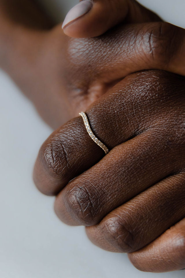 Close up of model hand wearing the curved Caia womens wedding band by Fluid Jewellery in yellow gold